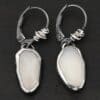 "Gracie" Earrings. The earrings are oval rose cut moonstones hanging vertically. There are silver leverback ear wires with silver wire wrapped around part of them.