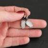 "Gracie" Earrings. The earrings are oval rose cut moonstones hanging vertically. There are silver leverback ear wires with silver wire wrapped around part of them. Earrings are held in the fingertips of a hand.
