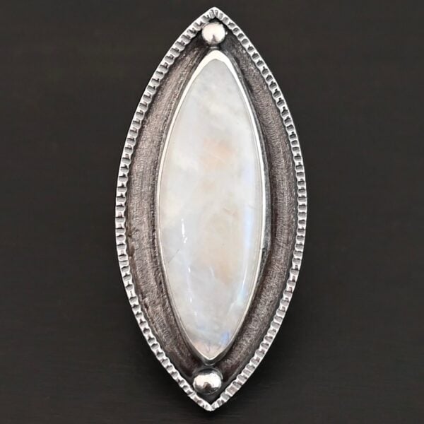 "Artemis Ring" The ring is large, marquise, vertical moonstone. There is a ball of silver on the top and bottom of it. There is textured silver around it, and a thin layer around that which is hammered.