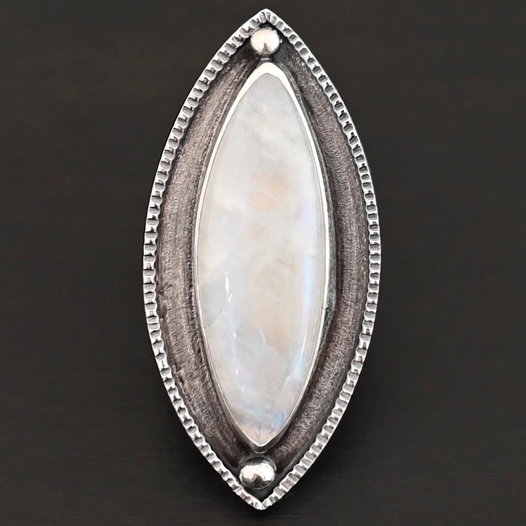 Artemis Ring "Artemis Ring" The ring is large, marquise, vertical moonstone. There is a ball of silver on the top and bottom of it. There is textured silver around it, and a thin layer around that which is hammered.