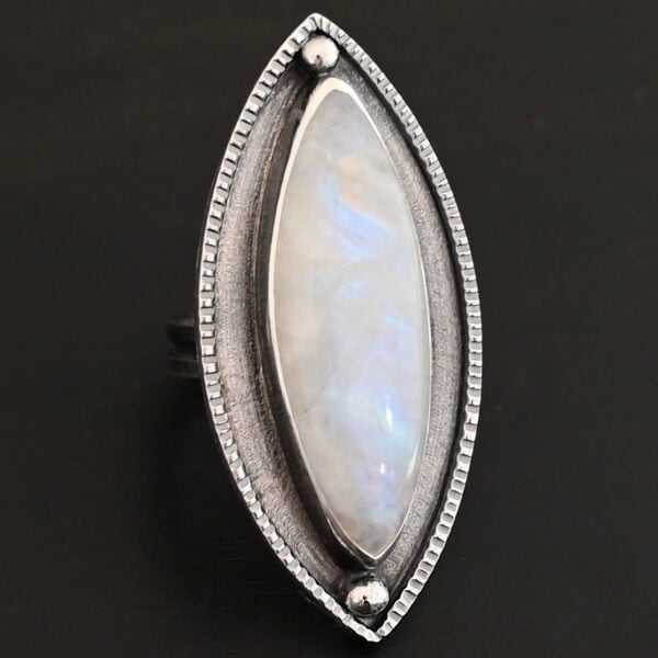 "Artemis Ring" The ring is large, marquise, vertical moonstone. There is a ball of silver on the top and bottom of it. There is textured silver around it, and a thin layer around that which is hammered.