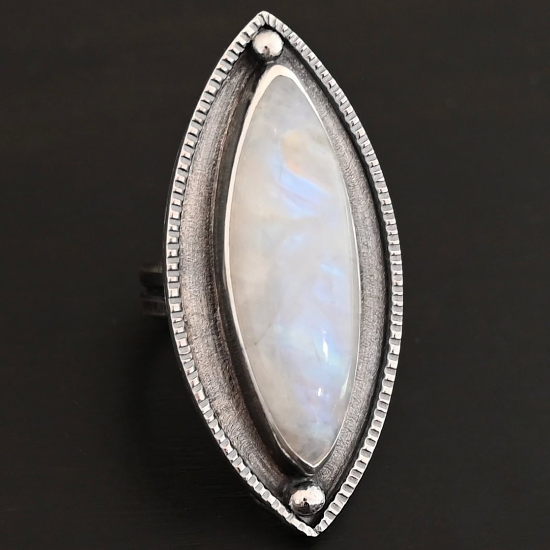 Artemis Ring "Artemis Ring" The ring is large, marquise, vertical moonstone. There is a ball of silver on the top and bottom of it. There is textured silver around it, and a thin layer around that which is hammered.
