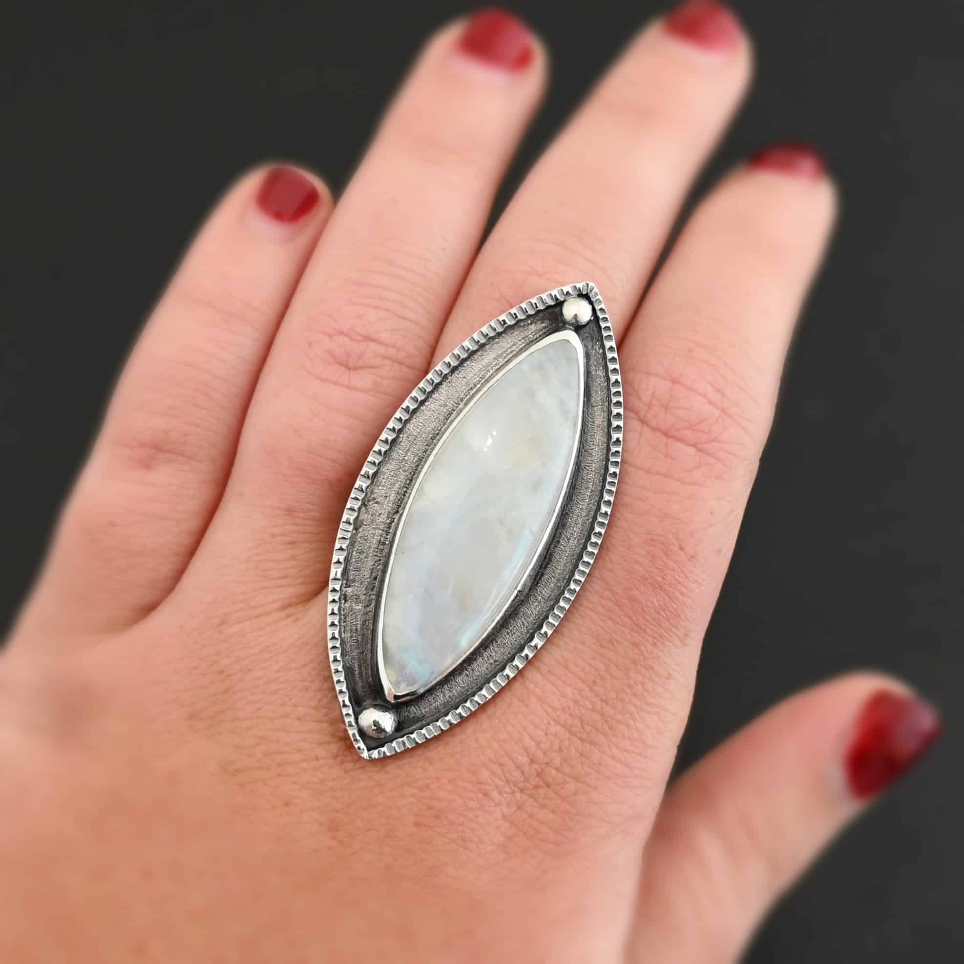 Artemis Ring "Artemis Ring" The ring is large, marquise, vertical moonstone. There is a ball of silver on the top and bottom of it. There is textured silver around it, and a thin layer around that which is hammered.