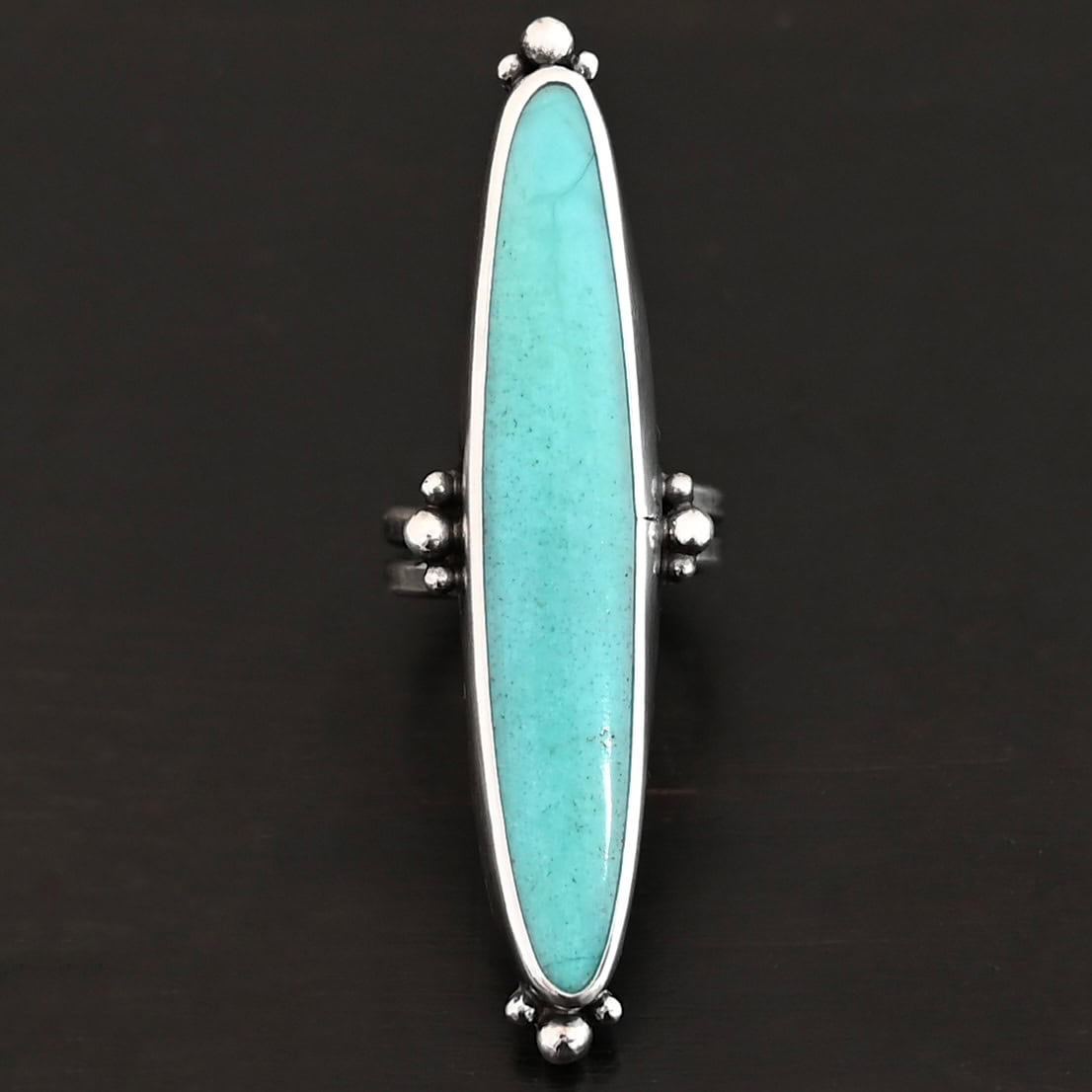"Abilene" Ring. It is a long, oval, vertical turquoise. There are four groups of three balls of silver around the ring. Three are on the top, three on the bottom, and on the left and right side.