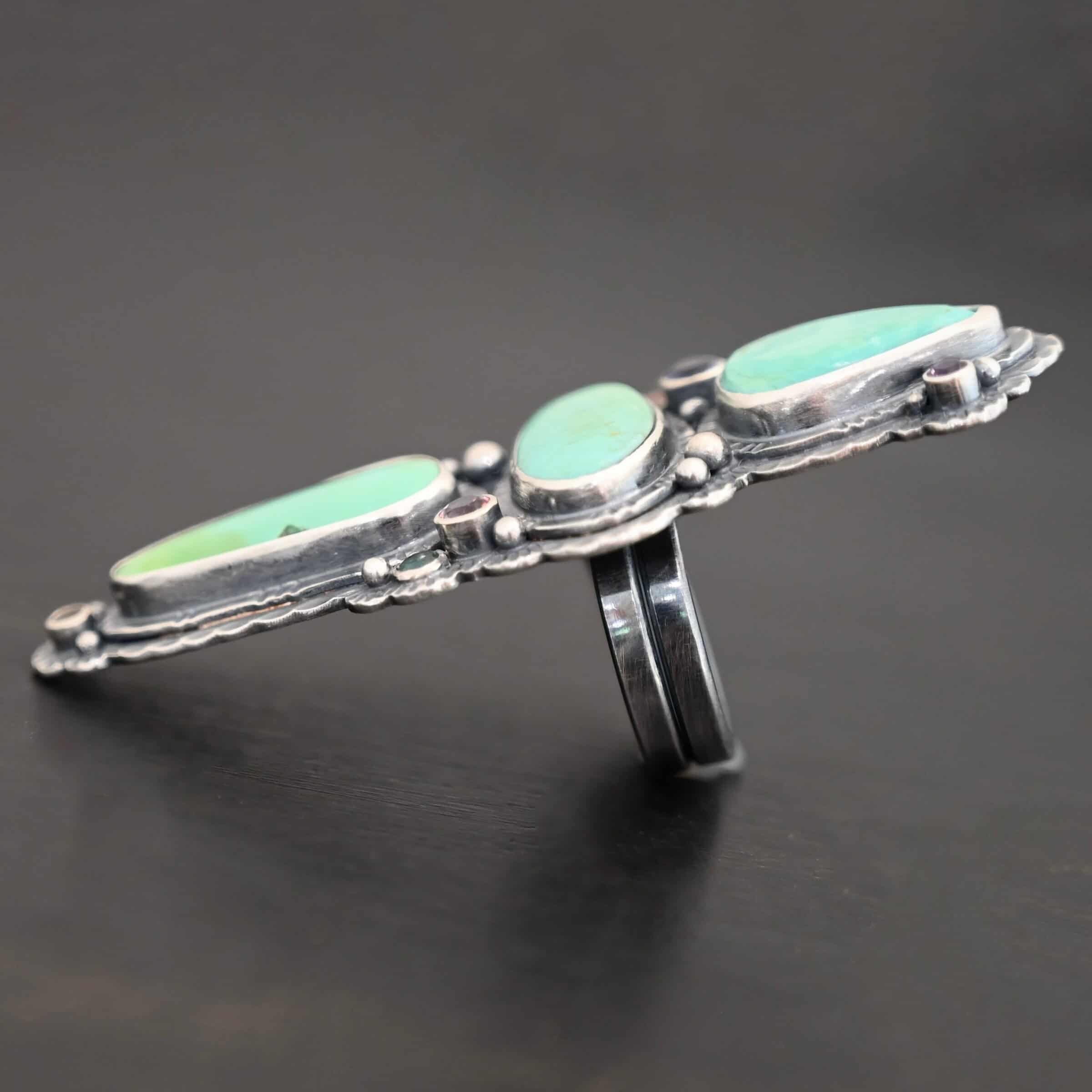 "Western Flowers" Ring. There are three oval turquoise. The one on the top and bottom are vertical, and the one in between is horizontal. They are all a larger size. There are six other, smaller circular stones scattered around the turquoise. There are two layers of hammered silver around all of the stones.