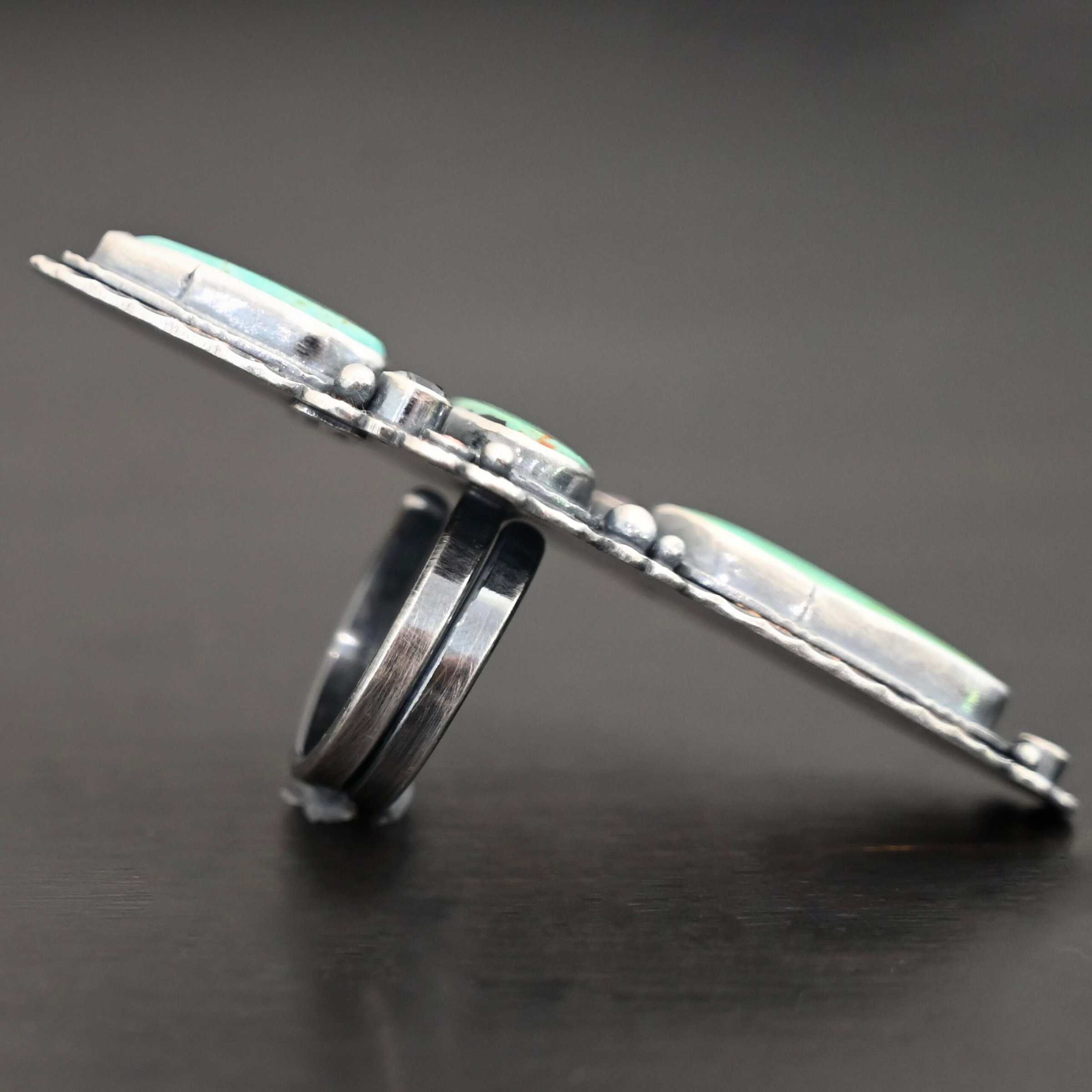 "Western Flowers" Ring. There are three oval turquoise. The one on the top and bottom are vertical, and the one in between is horizontal. They are all a larger size. There are six other, smaller circular stones scattered around the turquoise. There are two layers of hammered silver around all of the stones.