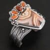 "Something In The Orange" Cuff. Sterling Silver, Teepee Canyon Agate, and Orange Kyanite. There is a large, wide, trapezoid agate on the bottom with four orange kyanites going across it on the top. Three are marquise shaped and one is a circular shape. The cuff band is very wide, and has lines of silver that are wavy and go across it. There is silver ball detail around the rest of the cuff.