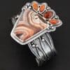 "Something In The Orange" Cuff. Sterling Silver, Teepee Canyon Agate, and Orange Kyanite. There is a large, wide, trapezoid agate on the bottom with four orange kyanites going across it on the top. Three are marquise shaped and one is a circular shape. The cuff band is very wide, and has lines of silver that are wavy and go across it. There is silver ball detail around the rest of the cuff.