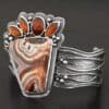 "Something In The Orange" Cuff. Sterling Silver, Teepee Canyon Agate, and Orange Kyanite. There is a large, wide, trapezoid agate on the bottom with four orange kyanites going across it on the top. Three are marquise shaped and one is a circular shape. The cuff band is very wide, and has lines of silver that are wavy and go across it. There is silver ball detail around the rest of the cuff.