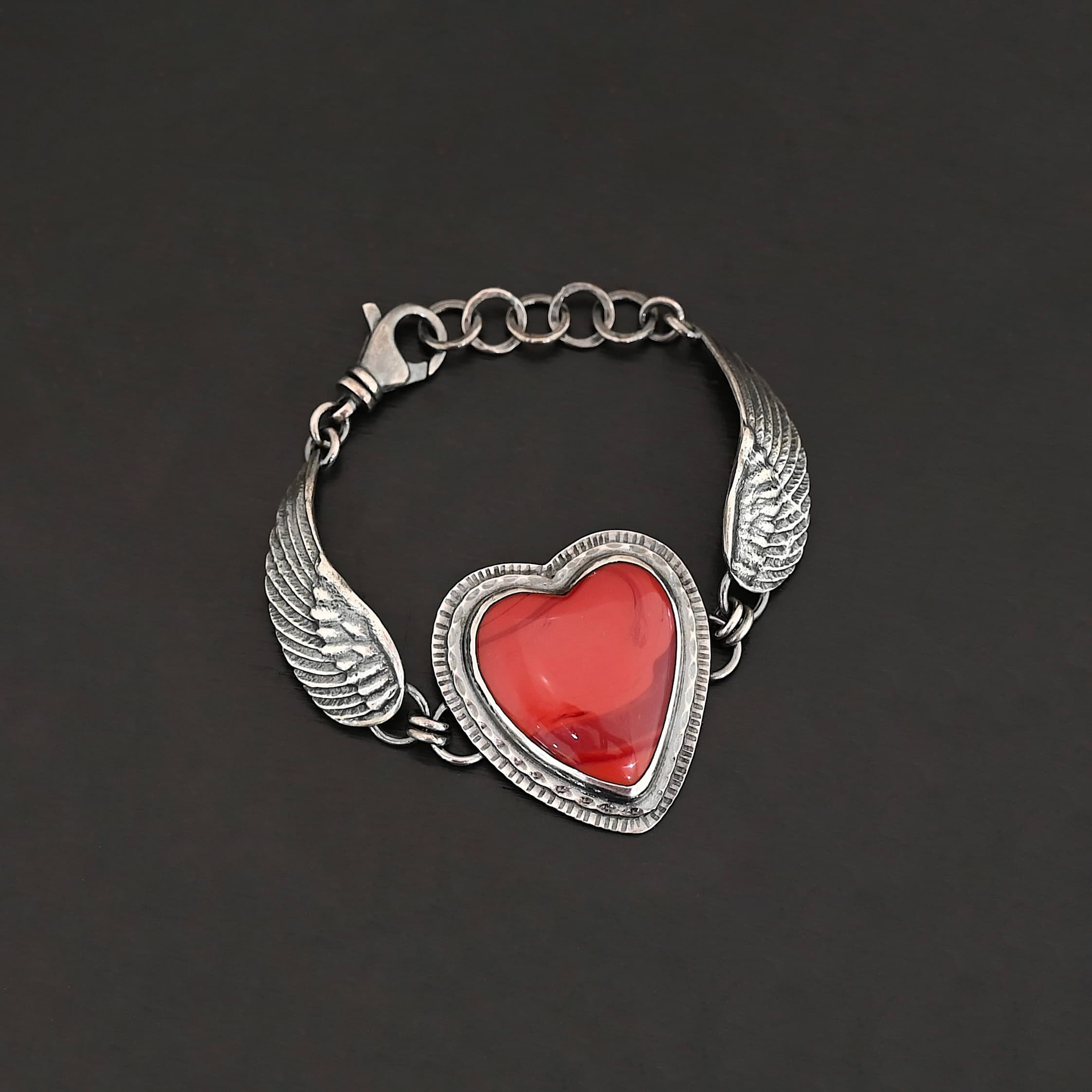 "Cerise" Bracelet. The bracelet is a rosarita heart with medium sized angel wings on each side. The angel wings curve lightly so they can fit around the wrist. There is two layers of hammered sterling silver around the heart. Bracelet has a silver lobster claw clasp.