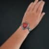 "Cerise" Bracelet. The bracelet is a rosarita heart with medium sized angel wings on each side. The angel wings curve lightly so they can fit around the wrist. There is two layers of hammered sterling silver around the heart. Bracelet has a silver lobster claw clasp. Bracelet is shown up close by a model on their wrist.