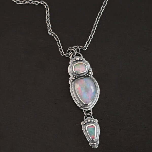 "Blue Moon Magic" Necklace. There are three opals in a line down. The top one is a small horizontal oval. The next one is a larger, vertical opal. The bottom one is a small triangle. Each one has silver ball detail surrounding it, as well as hammered silver.