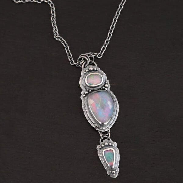 "Blue Moon Magic" Necklace. There are three opals in a line down. The top one is a small horizontal oval. The next one is a larger, vertical opal. The bottom one is a small triangle. Each one has silver ball detail surrounding it, as well as hammered silver.