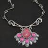 "In The Dawns" Necklace. There are six rubies and one large, wide, pear shaped red/pink opal pointing up. The opal is at the bottom, with five oval vertical rubies circling around the bottom of it. In between each ruby is a silver leaf and on the end of each ruby is a ball of silver. The clasp of the necklace has three silver leaves and a ball of silver above an oval ruby. Chain is handmade out of wavy links of sterling silver.