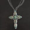 "Firm In Faith" Necklace. Necklace is a large cross shape with six oval turquoise creating the cross shaped eight small circular turquoise around the rest of the pendant. Chain is multiple strands that meet at the back.