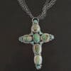 "Firm In Faith" Necklace. Necklace is a large cross shape with six oval turquoise creating the cross shape eight small circular turquoise around the rest of the pendant. Chain is multiple strands that meet at the back.