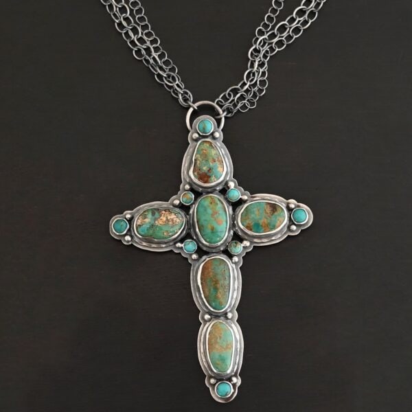 "Firm In Faith" Necklace. Necklace is a large cross shape with six oval turquoise creating the cross shape eight small circular turquoise around the rest of the pendant. Chain is multiple strands that meet at the back.
