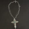 "Firm In Faith" Necklace. Necklace is a large cross shape with six oval turquoise creating the cross shape and eight small circular turquoise around the rest of the pendant. Chain is multiple strands that meet at the back. Necklace has a small silver cross with a turquoise in the center of it for the clasp.