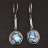 "Seven Summers Ago" Earrings. Each earring has a short line of vertical silver with silver wire wrapped around the bottom of it. Soldered to the bottom of the line is a circular turquoise with smooth silver around it. The wire is wrapped above the turquoise.