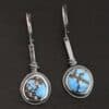 "Simmered In Sunshine" Earrings. Each earring has a short line of vertical silver with silver wire wrapped around the bottom of it. Soldered to the bottom of the line is a circular turquoise with smooth silver around it. The wire is wrapped above the turquoise.