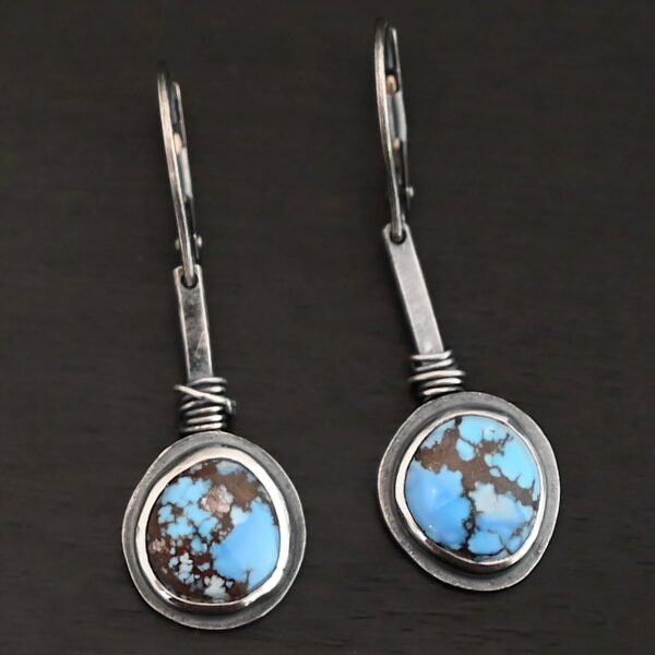 "Simmered In Sunshine" Earrings. Each earring has a short line of vertical silver with silver wire wrapped around the bottom of it. Soldered to the bottom of the line is a circular turquoise with smooth silver around it. The wire is wrapped above the turquoise.