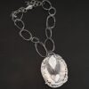 Back of the "Back To Our Roots" Necklace. There is a loop at the top and a marquise shape beneath it with the words, "You already know my heart" stamped into it. There is an angel wing on each side of the marquise shape. There is a small garnet in between the angel wings on the bottom. Beneath this is a hammered heart. Beneath that is a curved piece that says, "Wild Prairie Silver."