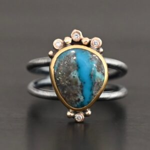 "Kingdom In The Sky" Ring. there is a circular turquoise in the center with three diamonds on the top of it and one on the bottom. There are four balls of gold on top of it, one on each end and two in between, and two balls of gold on the bottom, one on each side of the diamond. Ring band is two lines of silver, one soldered to the top and one to the bottom. They meet at the back of the ring and leave the center empty.