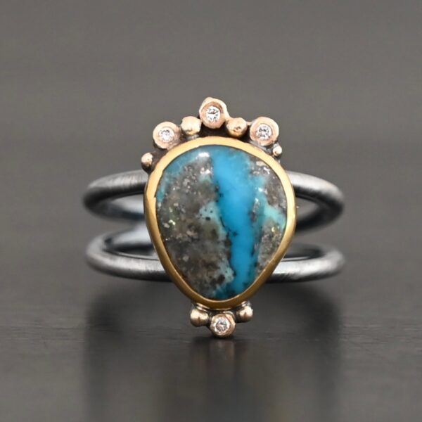 "Kingdom In The Sky" Ring. there is a circular turquoise in the center with three diamonds on the top of it and one on the bottom. There are four balls of gold on top of it, one on each end and two in between, and two balls of gold on the bottom, one on each side of the diamond. Ring band is two lines of silver, one soldered to the top and one to the bottom. They meet at the back of the ring and leave the center empty.