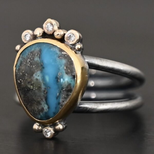 "Kingdom In The Sky" Ring. there is a circular turquoise in the center with three diamonds on the top of it and one on the bottom. There are four balls of gold on top of it, one on each end and two in between, and two balls of gold on the bottom, one on each side of the diamond. Ring band is two lines of silver, one soldered to the top and one to the bottom. They meet at the back of the ring and leave the center empty.