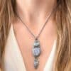 "Blue Moon Magic" Necklace. There are three opals in a line down. The top one is a small horizontal oval. The next one is a larger, vertical opal. The bottom one is a small triangle. Each one has silver ball detail surrounding it, as well as hammered silver. Necklace is shown up close by a model wearing it.