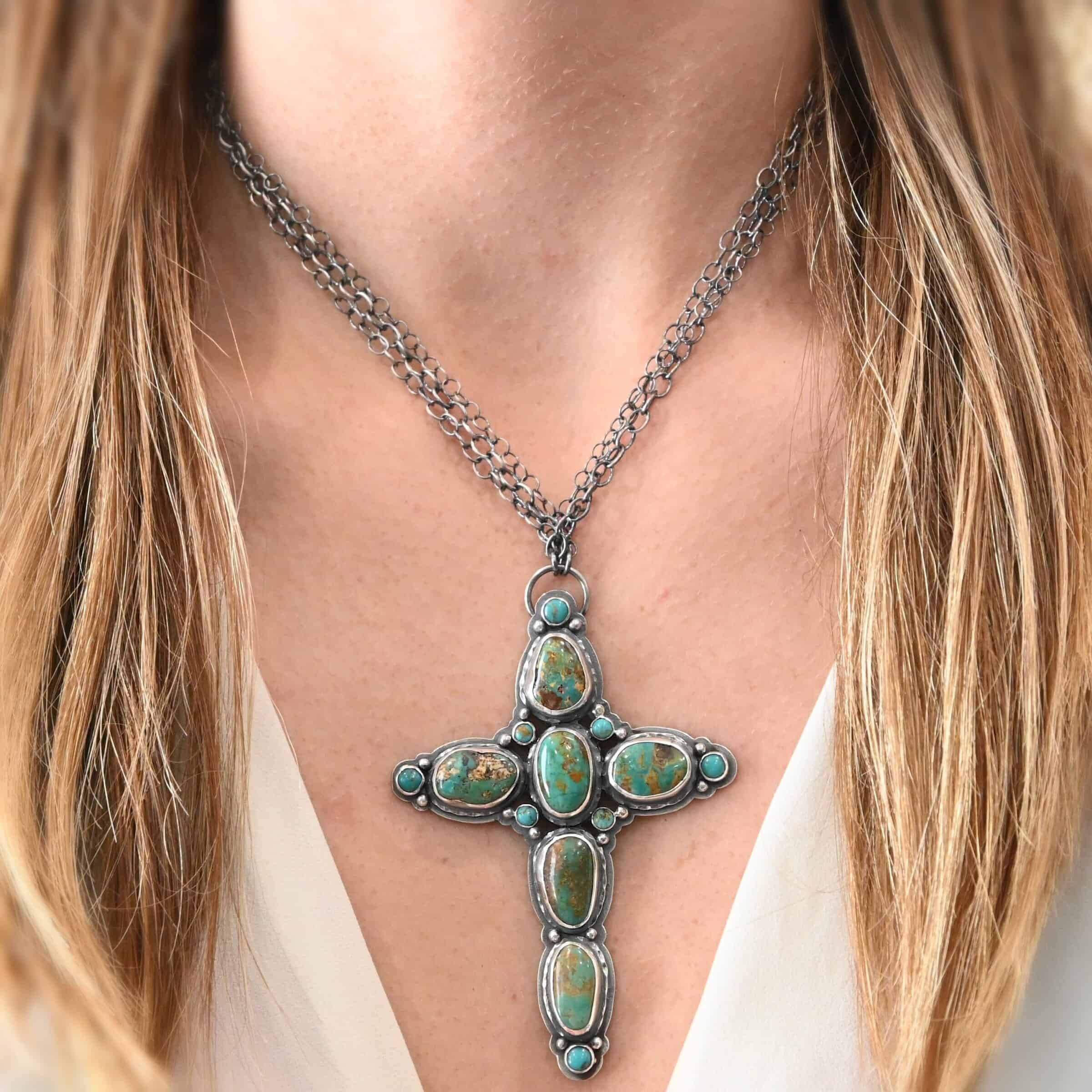 Firm In Faith Necklace "Firm In Faith" Necklace. Necklace is a large cross shape with six oval turquoise creating the cross shape and eight small circular turquoise around the rest of the pendant. Chain is multiple strands that meet at the back. Necklace is shown up close by a model.