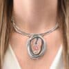 "Try Something New" Necklace. There is a medium sized, oval crazy lace agate in the center. There are multiple lines of silver wrapping around it, but not touching the stone. There is hammered silver and silver ball detail. Pendant is soldered to three large, curved bars of silver that sit around the throat.