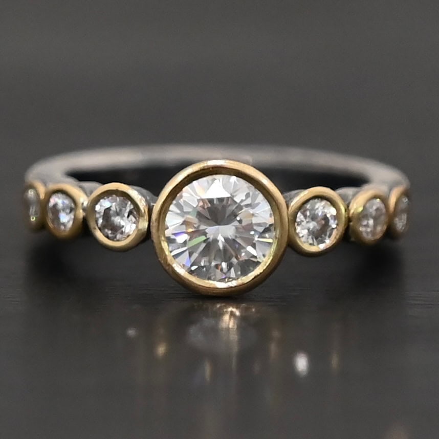 "Diana" Ring. There is two carat moissanite in the center of the ring, with six more smaller moissanites, three on each side of the center one. Each stone is set in gold. The ring band is silver.