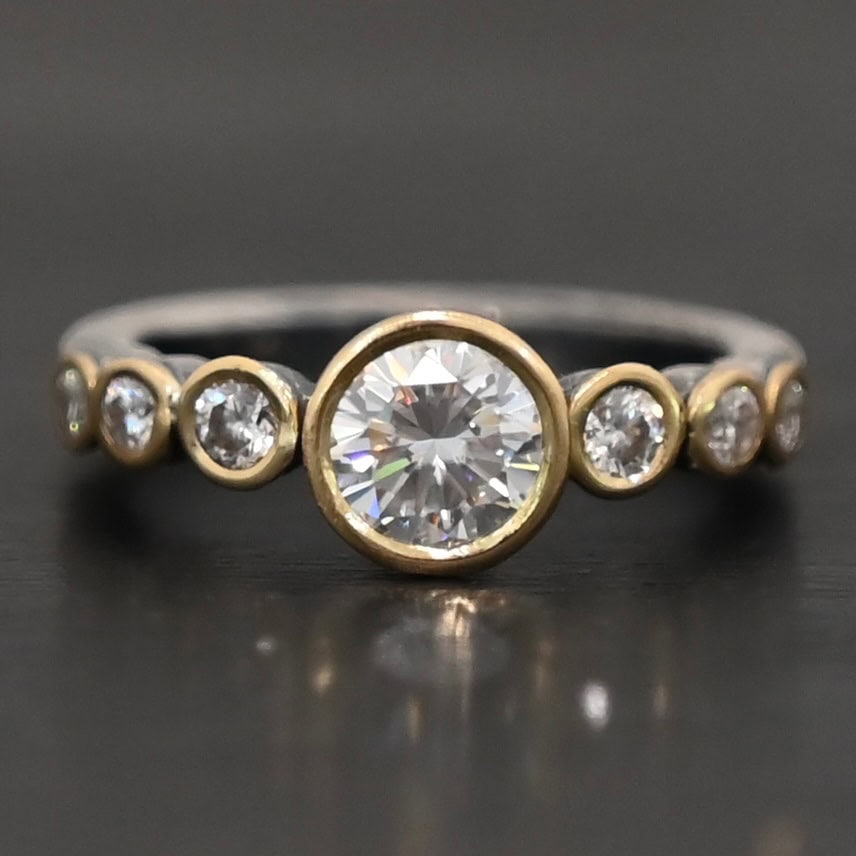 "Diana" Ring. There is two carat moissanite in the center of the ring, with six more smaller moissanites, three on each side of the center one. Each stone is set in gold. The ring band is silver.