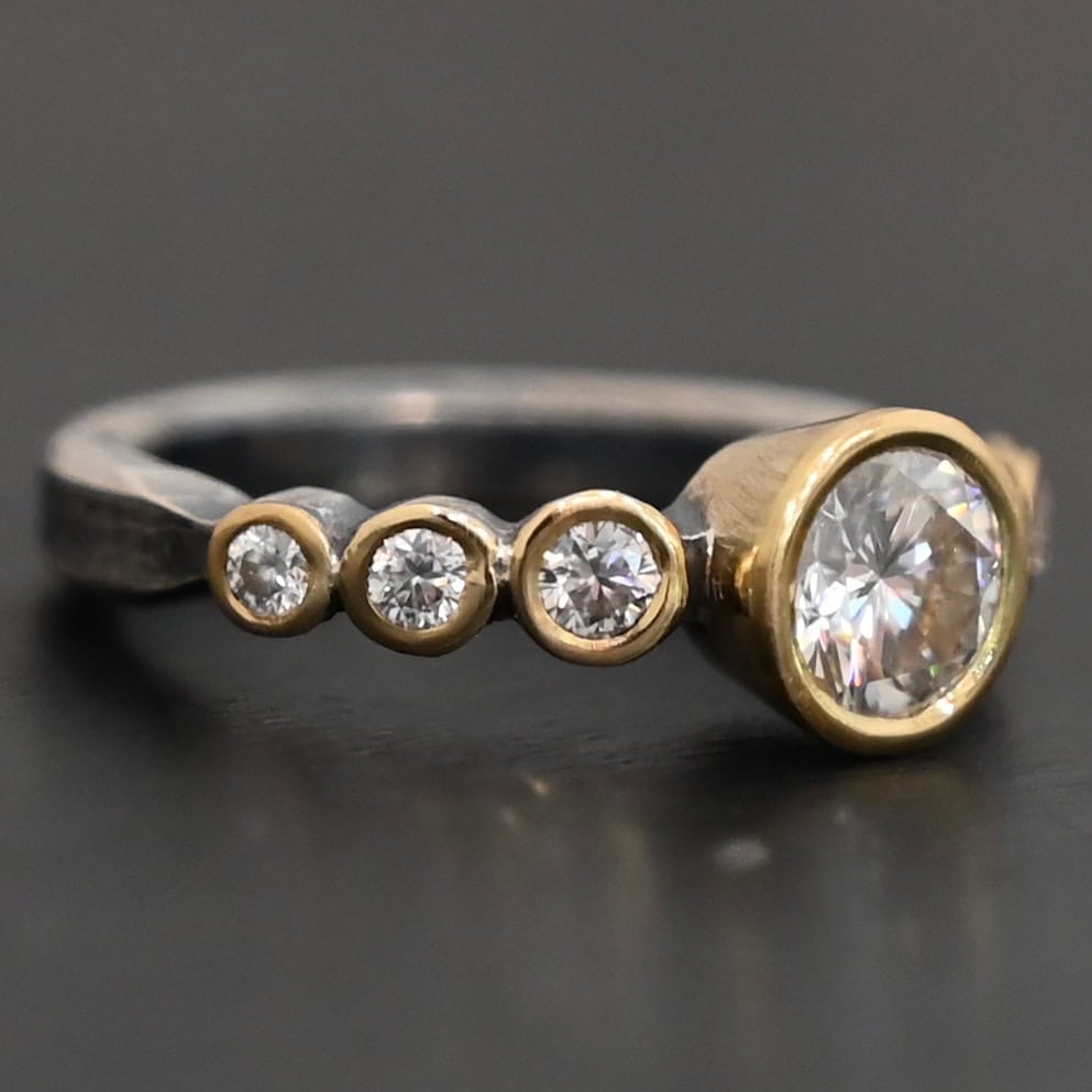"Diana" Ring. There is two carat moissanite in the center of the ring, with six more smaller moissanites, three on each side of the center one. Each stone is set in gold. The ring band is silver.