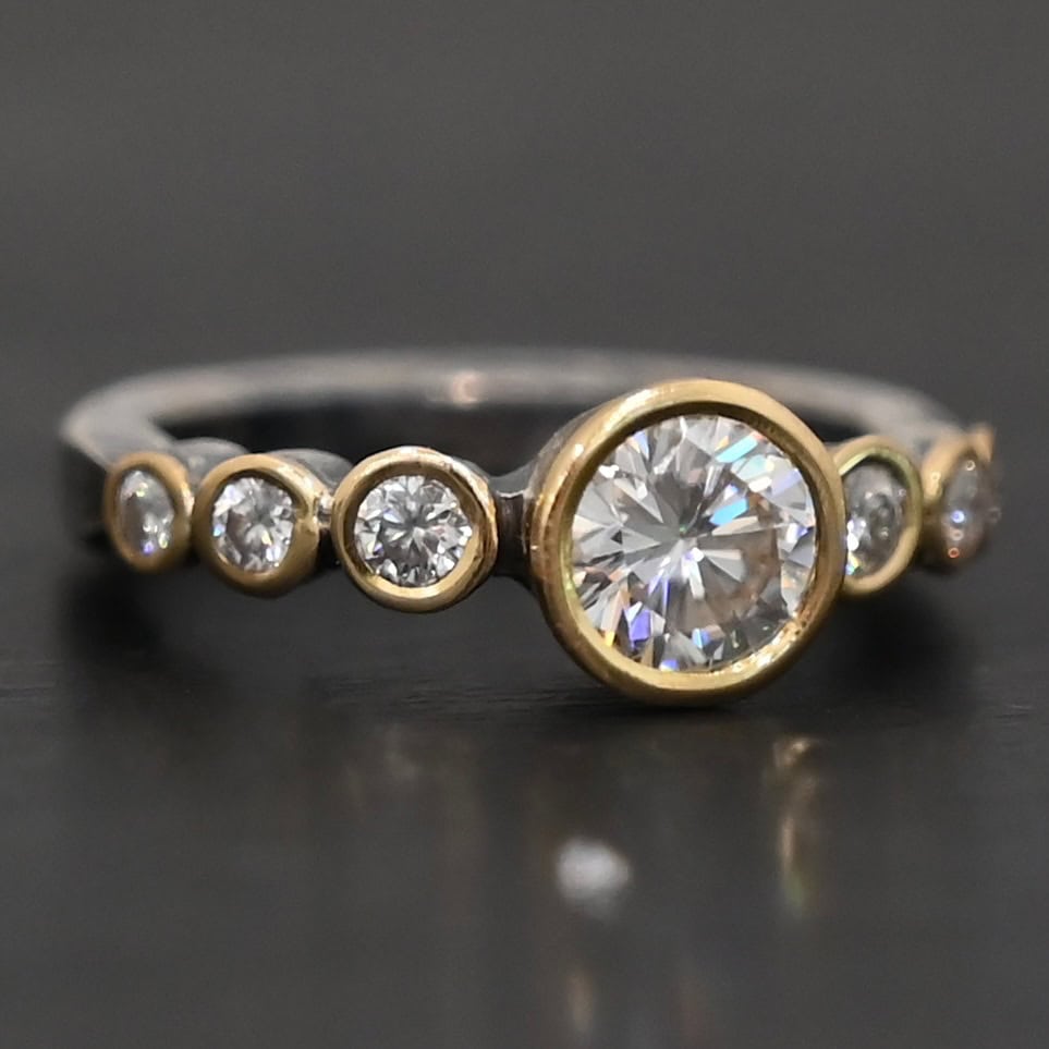 "Diana" Ring. There is two carat moissanite in the center of the ring, with six more smaller moissanites, three on each side of the center one. Each stone is set in gold. The ring band is silver.