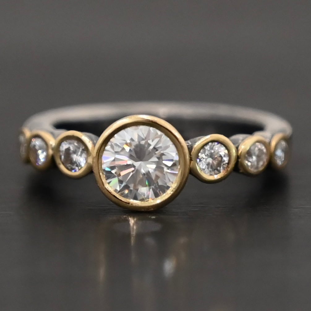 "Diana" Ring. There is two carat moissanite in the center of the ring, with six more smaller moissanites, three on each side of the center one. Each stone is set in gold. The ring band is silver.