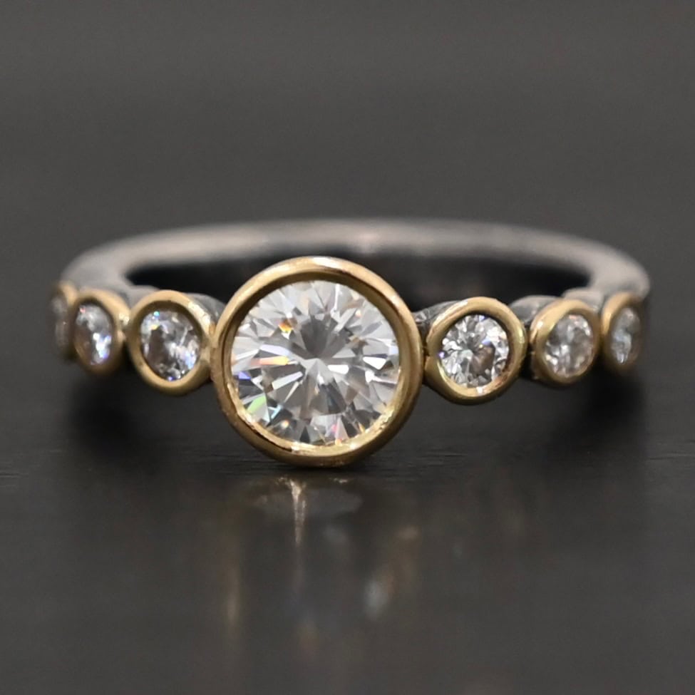 "Diana" Ring. There is two carat moissanite in the center of the ring, with six more smaller moissanites, three on each side of the center one. Each stone is set in gold. The ring band is silver.