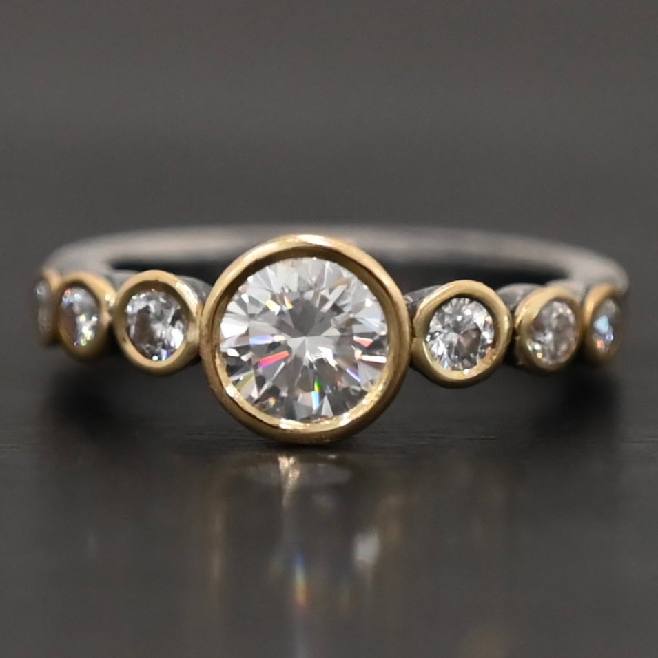 "Diana" Ring. There is two carat moissanite in the center of the ring, with six more smaller moissanites, three on each side of the center one. Each stone is set in gold. The ring band is silver.