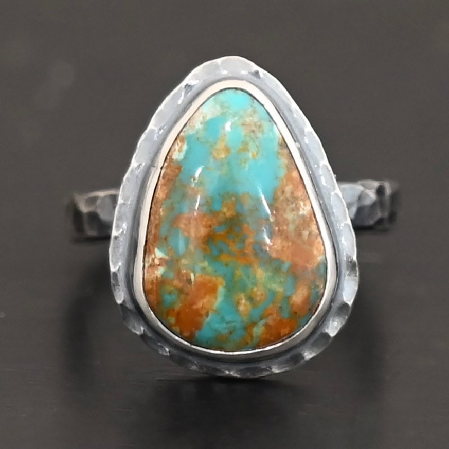 Elias Ring "Elias" Ring. There is a teardrop shaped turquoise in the center with hammered sterling silver around it. Ring is set against a black background.