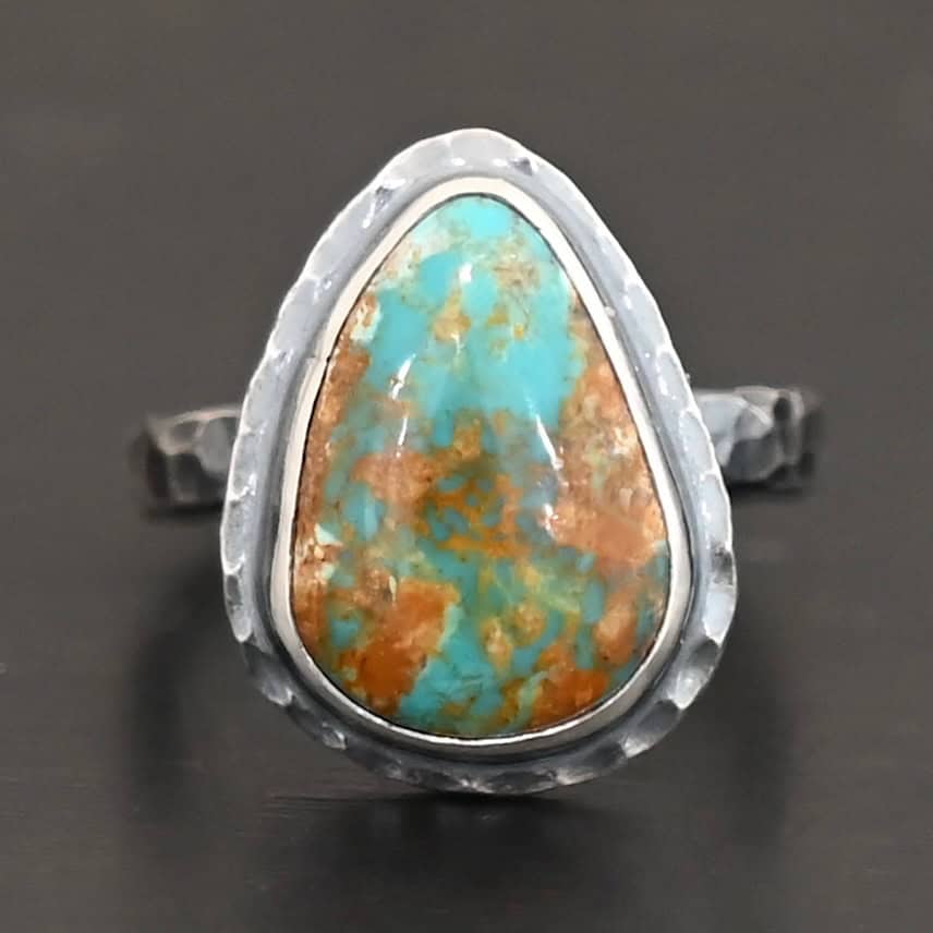Elias Ring "Elias" Ring. There is a teardrop shaped turquoise in the center with hammered sterling silver around it. Ring is set against a black background.