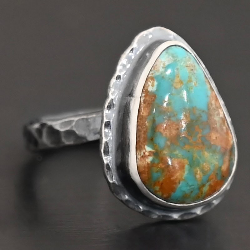 Elias Ring "Elias" Ring. There is a teardrop shaped turquoise in the center with hammered sterling silver around it. Ring is set against a black background.
