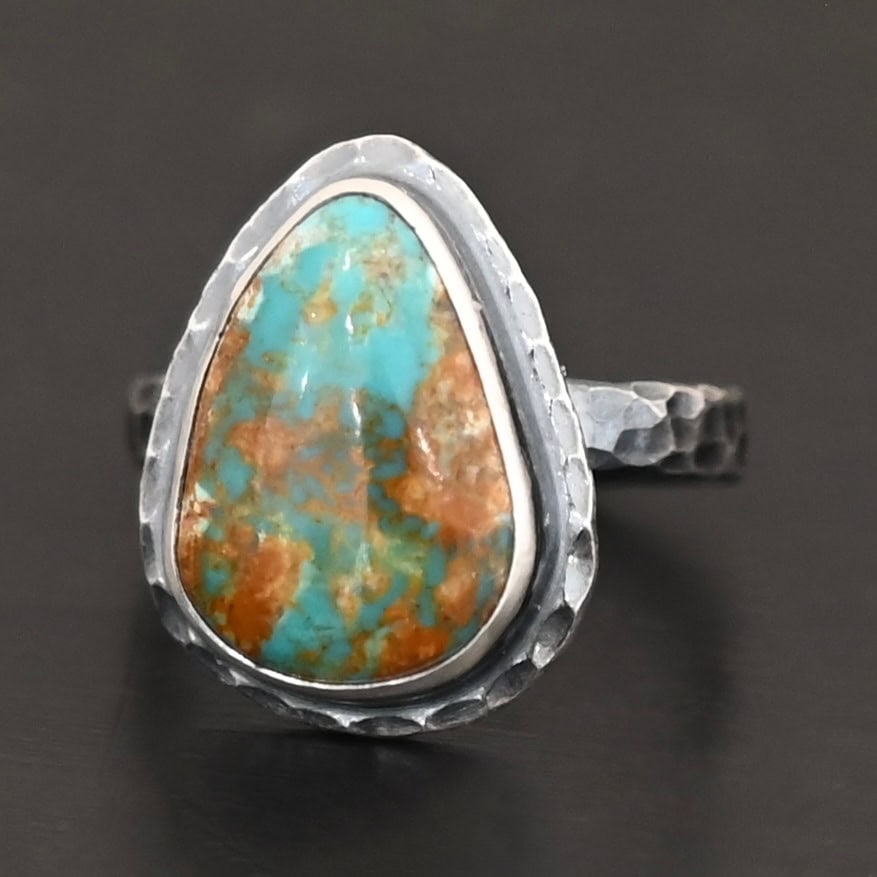 Elias Ring "Elias" Ring. There is a teardrop shaped turquoise in the center with hammered sterling silver around it. Ring is set against a black background.