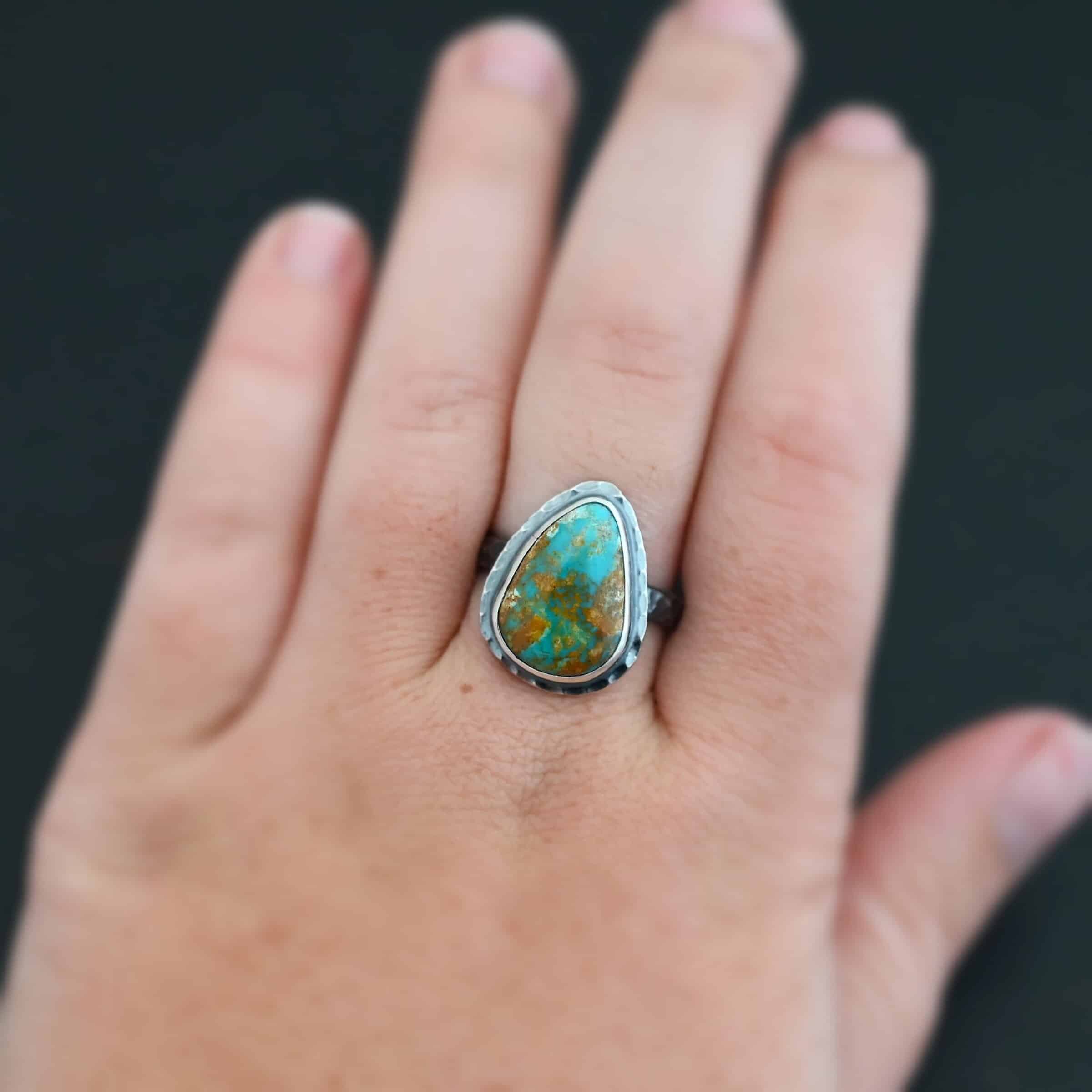 Elias Ring "Elias" Ring. There is a teardrop shaped turquoise in the center with hammered sterling silver around it. Ring is shown up close by a model.