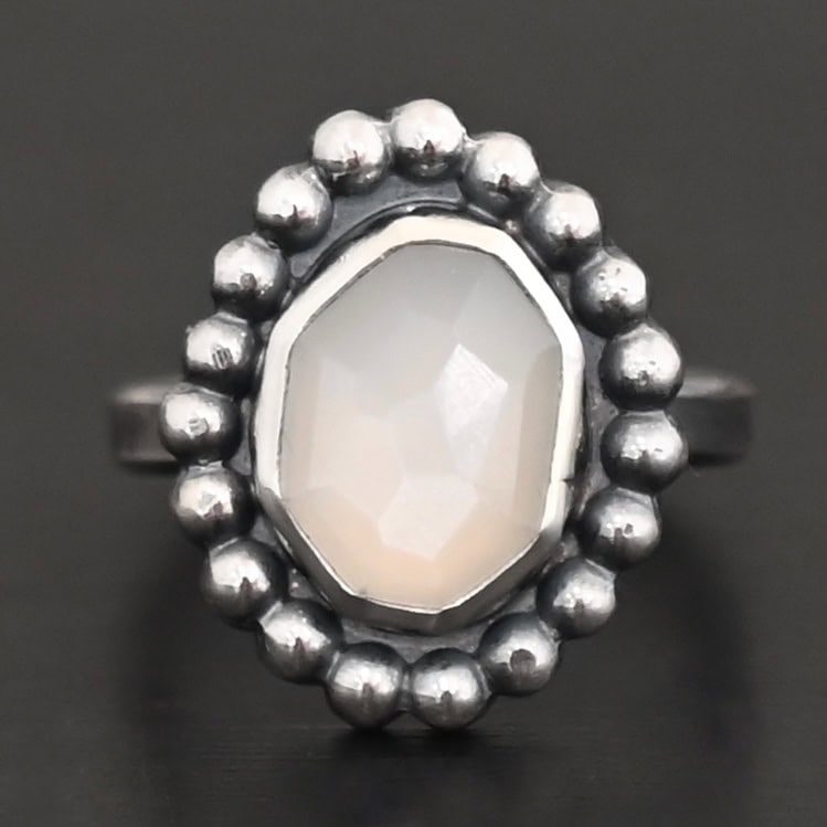 "Adelina" Ring. Sterling Silver & Moonstone. There is an oval, vertical moonstone in the center with balls of silver circling all the way around it. Ring band is smooth & lightly oxidized.