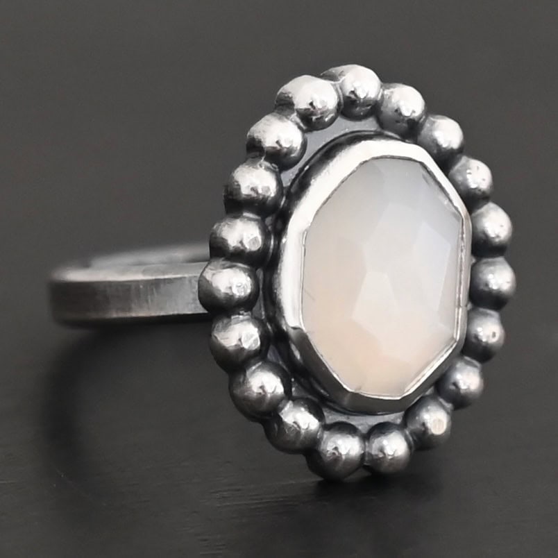 "Adelina" Ring. Sterling Silver & Moonstone. There is an oval, vertical moonstone in the center with balls of silver circling all the way around it. Ring band is smooth & lightly oxidized.