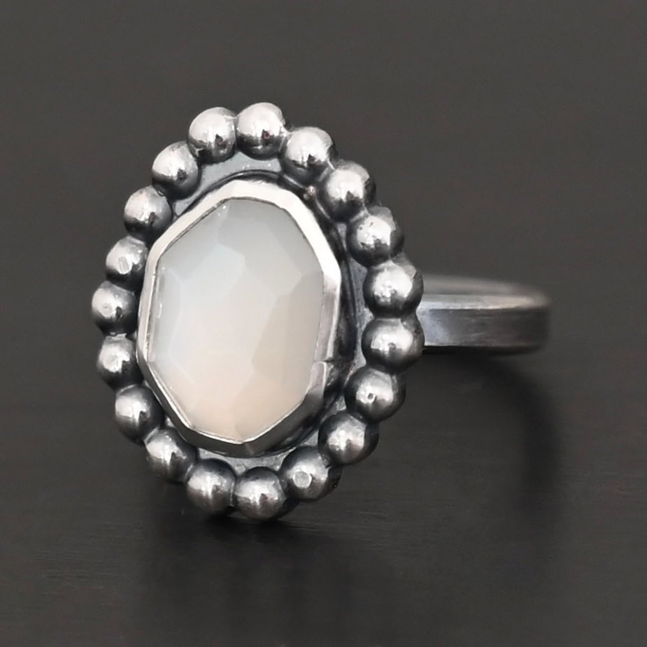 "Adelina" Ring. Sterling Silver & Moonstone. There is an oval, vertical moonstone in the center with balls of silver circling all the way around it. Ring band is smooth & lightly oxidized.