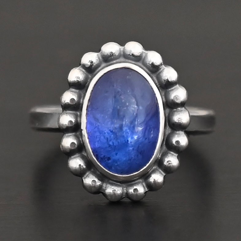 "Asena" Ring. Sterling Silver & Tanzanite. There is an oval, vertical tanzanite in the center with balls of silver circling all the way around it. Ring band is smooth & lightly oxidized.