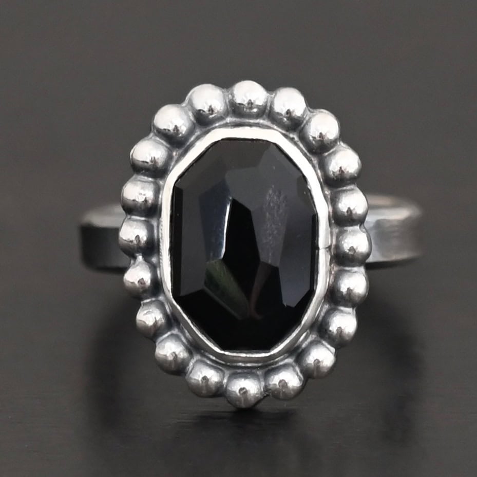 "Midnight Skies" Ring. Sterling Silver & Black Onyx. There is an oval, vertical black onyx in the center with balls of silver circling all the way around it. Ring band is smooth & lightly oxidized.