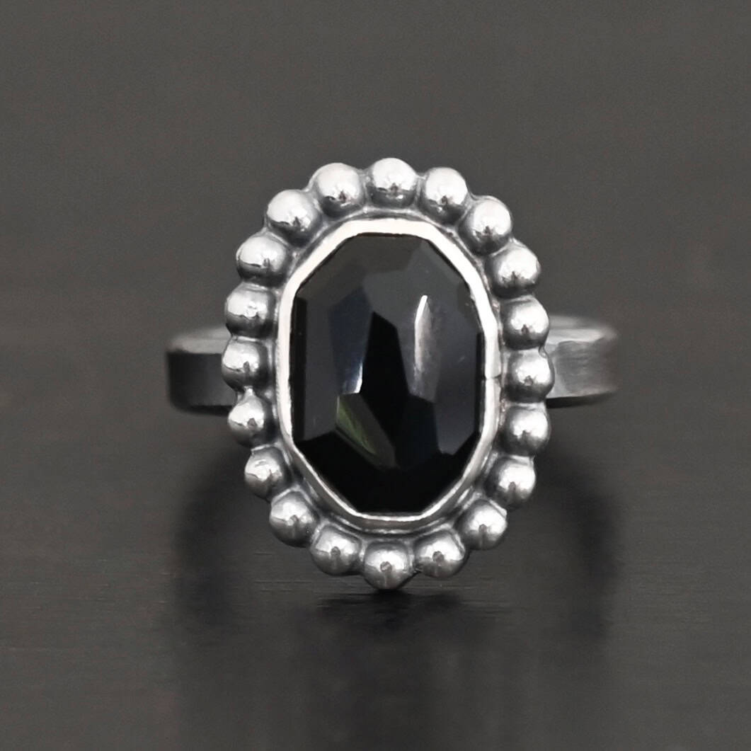 "Midnight Skies" Ring. Sterling Silver & Black Onyx. There is an oval, vertical black onyx in the center with balls of silver circling all the way around it. Ring band is smooth & lightly oxidized.
